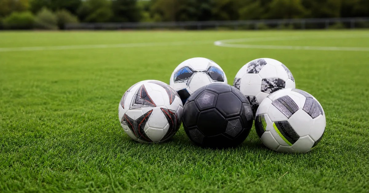 Five match and training footballs arranged on a grass pitch